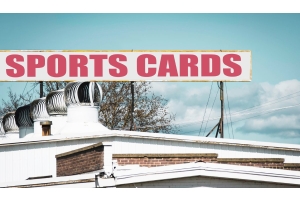 A red, white, and yellow retail sign on top of a white building that reads "SPORTS CARDS" against a clear blue sky.