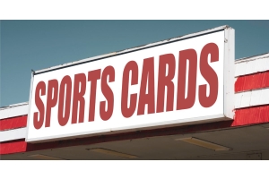 A white vintage sign with the words "Sports Cards” in large red letters. The sign is connected to a red and white awning.