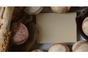 A baseball glove rests on a table with other baseballs surrounding a blank card.