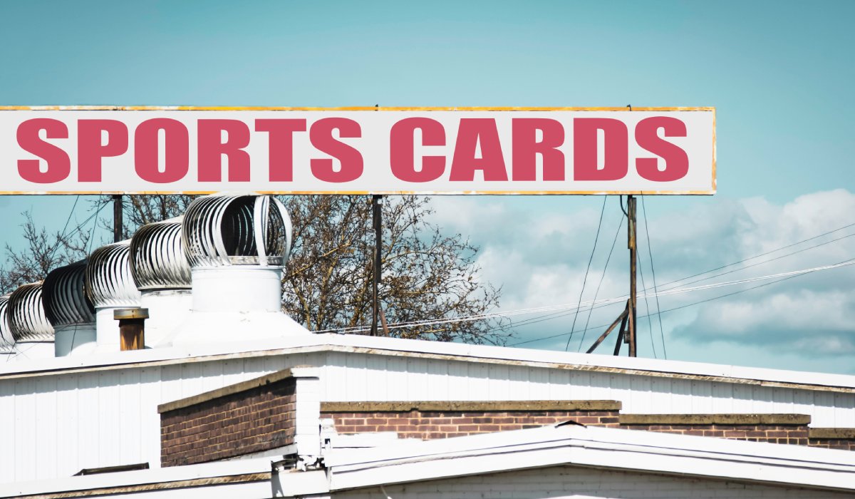 A red, white, and yellow retail sign on top of a white building that reads "SPORTS CARDS" against a clear blue sky.