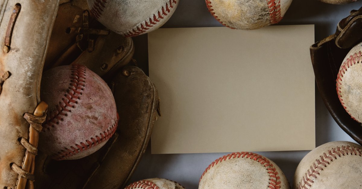A baseball glove rests on a table with other baseballs surrounding a blank card.
