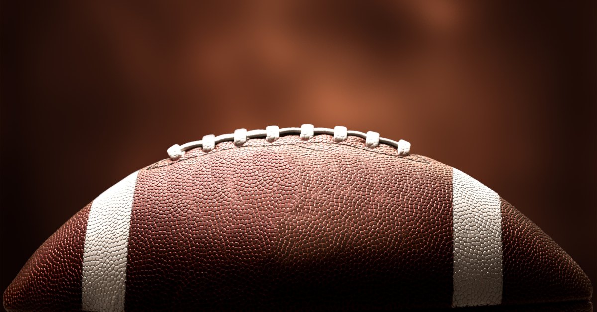 A side view of a pristine, new American football with white stripes and laces in front of a blurred, brown background.