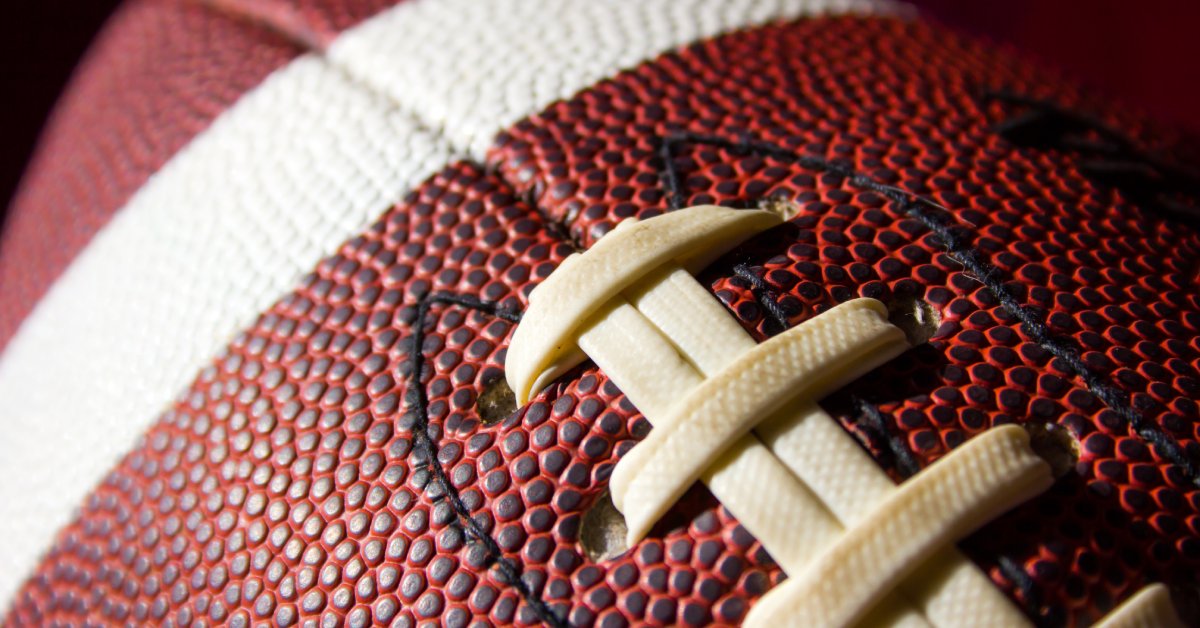 A close-up of brand-new American football with white laces, black stitching, and a white painted stripe.