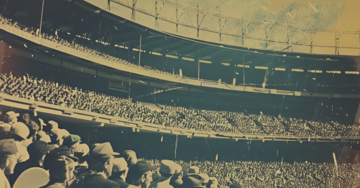A vintage photograph of an old sports stadium with three levels of seating. Every seat is filled with spectators.